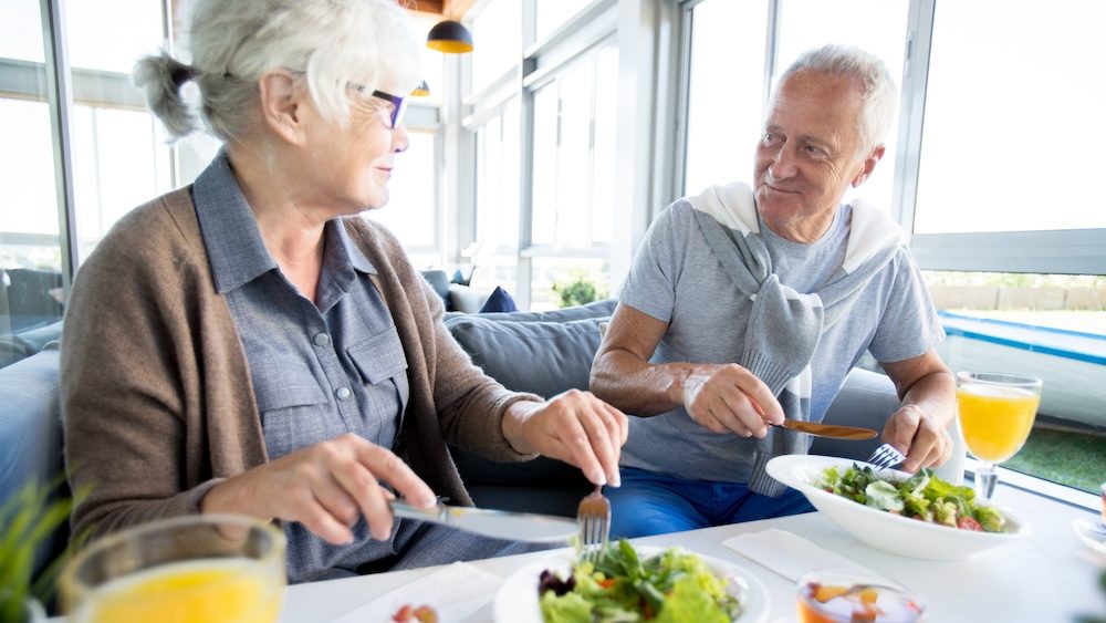 Portrait of modern senior couple enjoying lunch and conversation on vacation in resort cafe